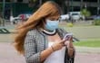En Venezuela, una mujer con mascarilla camina con su teléfono celular en la mano.