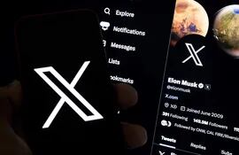 Un usuario sostiene un teléfono móvil que muestra el logotipo 'X' frente a una pantalla que muestra el perfil en esa misma red social de Elon Musk, en Los Ángeles, California (EE.UU.).
