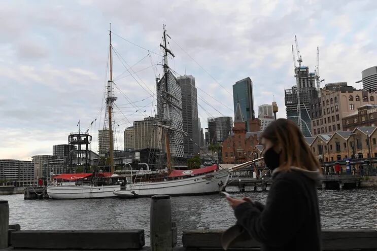 Una mujer con una máscara facial camina por el tranquilo puerto de Sydney el 19 de julio de 2021, en medio de un cierre en Melbourne y Sydney mientras Australia busca contener un aumento en los casos de coronavirus.