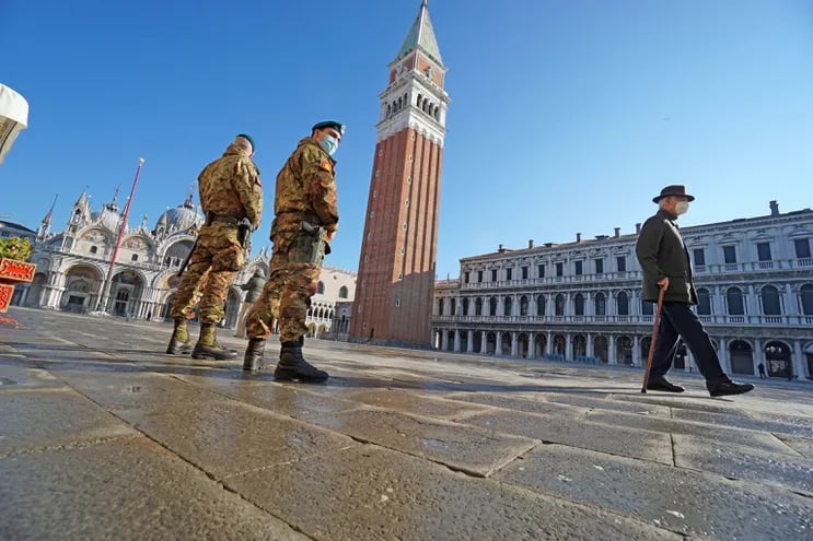 Dos soldados patrullando y un peatón con mascarilla son vistos en la plaza San Marco, en Venecia, Italia.