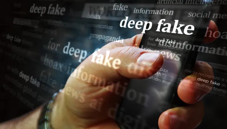 Una mano de hombre sostiene un teléfono celular. Un filtro se superpone con las palabras "deepfake", "hoax", "information", "disinformation".