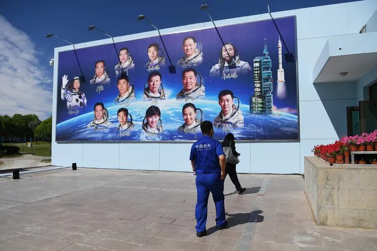 Un miembro del personal del Centro de Lanzamiento de Satélites de Jiuquan pasa junto a un tablero que muestra fotos de astronautas.