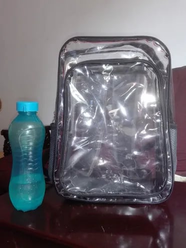 Mochila transparente con una botella con agua al lado.