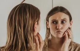 Una mujer se mira al espejo y no se muestra satisfecha con lo que ve