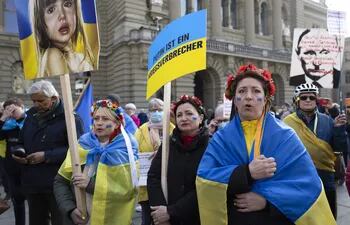 Manifestantes con banderas ucranianas cantan el himno nacional ucraniano durante una manifestación contra la invasión rusa frente al edificio del parlamento suizo en Berna, Suiza, el 19 de marzo de 2022.