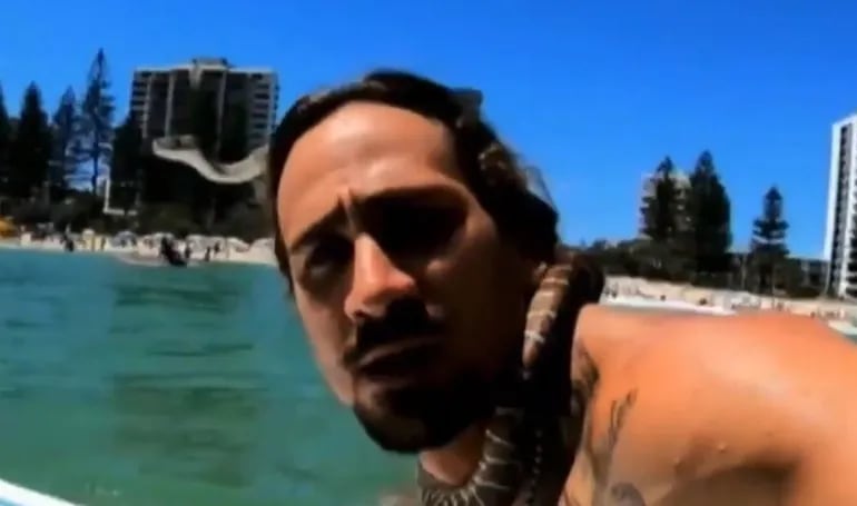 El surfista Higor Fiuza en una captura de pantalla sufeando con una serpiente pitón enroscada al cuello. El deportista recibió una multa de USD 1.500.