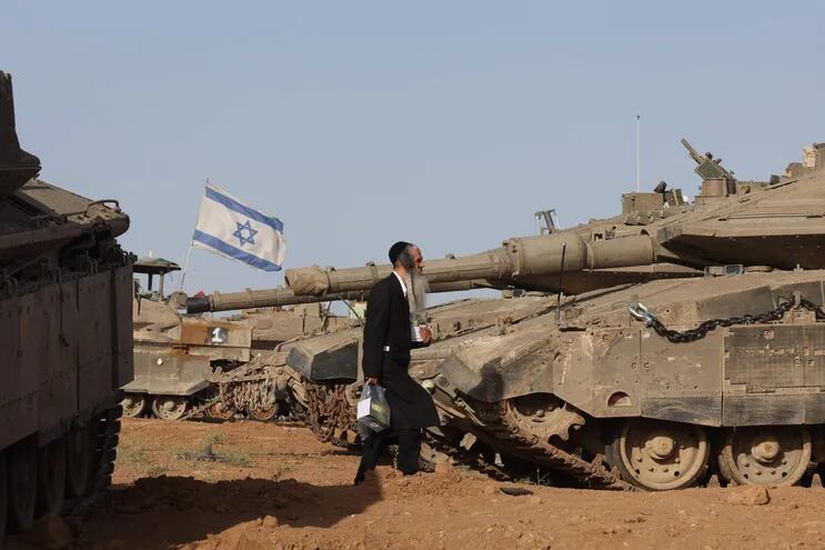Un judío ultraortodoxo pasa junto a vehículos militares israelíes reunidos cerca de la valla fronteriza con la Franja de Gaza.