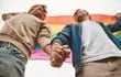 Imagen de referencia: dos personas agarrándose de la mano con una bandera del orgullo LGBTI de fondo.