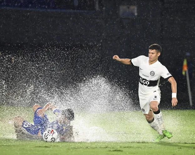 La pelota y el futbolista de Sol de América se pierden en la gran cantidad de agua levantada del gramado. Lo observa Paraguarí Espínola.