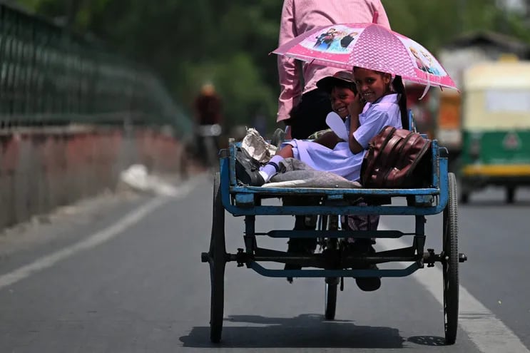 Los niños se refugian del sol bajo una sombrilla mientras viajan en la parte trasera de un carrito de bicicletas durante un caluroso día de verano en Nueva Delhi.