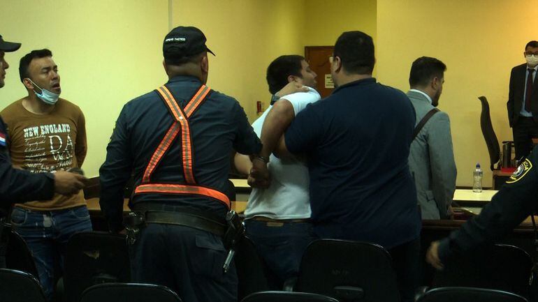Agentes policiales reducen a Gustavo Genes mientras este grita a los jueces, en la sala de juicio. A la izquierda, el condenado Erico Riquelme.