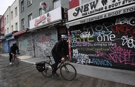 Dos ciclistas pasan frente a una hilera de  negocios cerrados de la calle Candem, en Londres, Inglaterra.