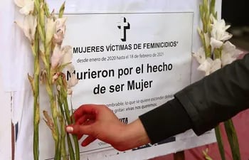Una persona coloca una flor cerca de un cartel en honor a las víctimas de feminicidios.