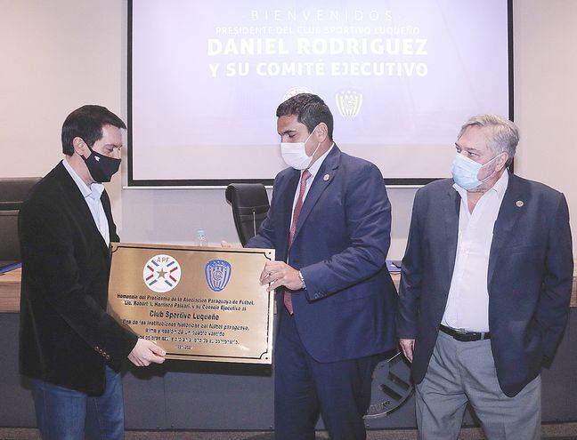 El nuevo titular del Sportivo Luqueño, Hugo Daniel Rodríguez, recibe la placa conmemorativa del centenario del presidente de la APF, Robert Harrison, y lo acompaña el Dr. Carlos Sosa Jovellanos.