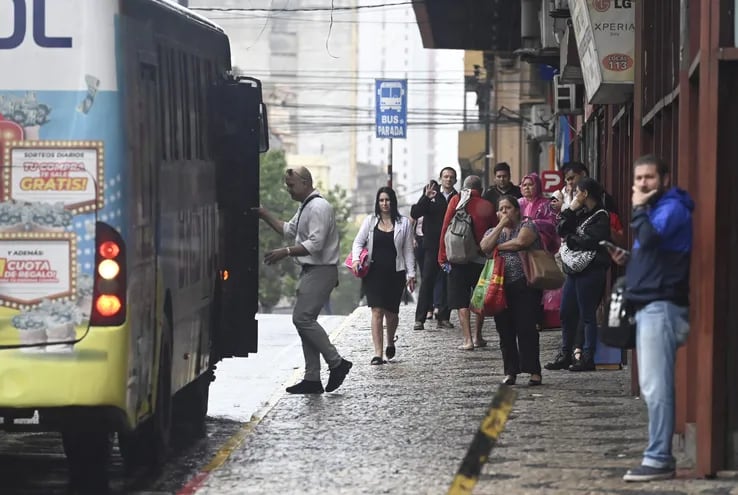Varias personas en una parada de buses en el microcentro de Asunción.