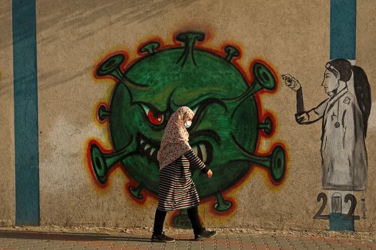 Una mujer pasa frente a un mural alusivo al virus de la covid-19 en la Ciudad de Gaza.