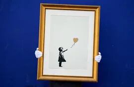 Un empleado de la casa de subastas Christie's sostiene una versión de la obra "Niña con globo" del artista Banksy en Londres, Reino Unido. Dos versiones de esta obra se subastarán del 11 al 24 de septiembre en Internet junto con otras obras de Banksy.