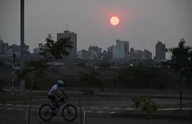 Un joven pedalea su bicicleta por la Costanera de Asunción. De fondo se ve la silueta de los edificios.