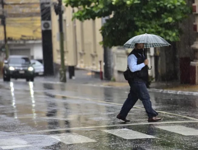 Un ciudadano cruza la calle en Asunción, que está cubierta de agua, con una sombrilla para protegerse de las precipitaciones.