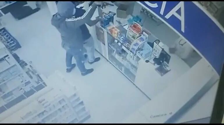 Uno de los ladrones apunta con un arma de fuego a las cajeras de la farmacia.