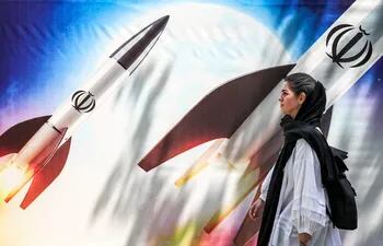 Una mujer camina frente a un mural que muestra misiles con el emblema de la República Islámica de Irán, en Teheran.