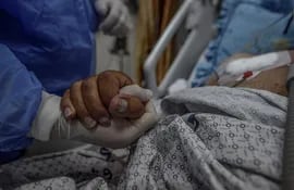 Un sanitario agarra la mano de un paciente en una unidad de cuidados intensivos.