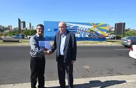 El artista Edward Hermosilla y el consejero de la Embajada de Alemania, Wolfgang Erdmannsdörfer, junto al mural "Levantando la paz" inaugurado en la Costanera de Asunción.