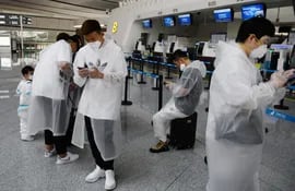 Gente vestida con trajes de protección esperan frente a los mostradores del aeropuerto Daxing en Pekín, China.