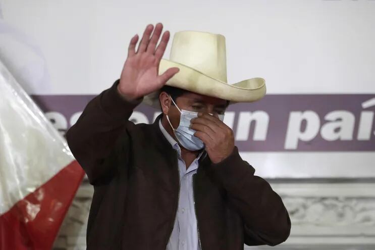 El candidato presidencial peruano Pedro Castillo saluda mientras acomoda su tapabocas durante una rueda de prensa.