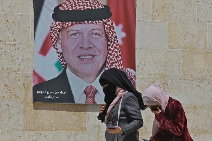 Dos mujeres caminan junto a un cartel con el retrato del rey Abdalá II de Jordania, en Amán.