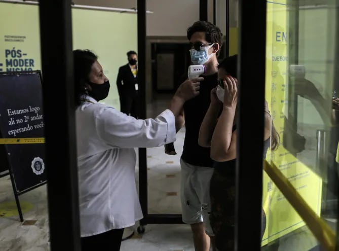 Una mujer toma la temperatura a visitantes del Centro Cultural Banco do Brasil, en Río de Janeiro (Brasil).  Los casos y muertes por covid van en descenso.