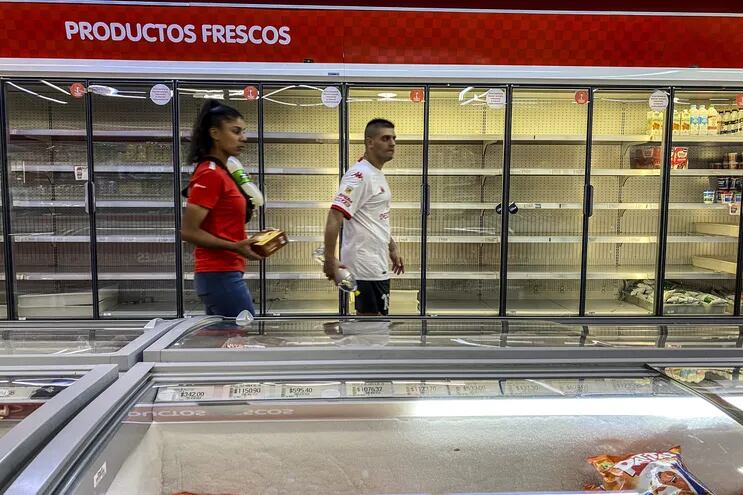 Dos personas caminan frente a las neveras casi vacías de un supermercado, en Buenos Aires (Argentina). Los precios al consumidor en Argentina experimentaron en febrero pasado una subida interanual del 102,5%, un 3,7% más que en enero último.  (EFE)