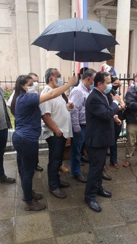Una mujer sostiene un paraguas para los senadores Richer y Pereira y para el diputado Vera Bejarano.