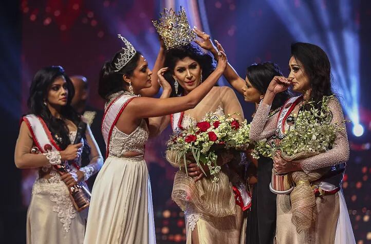 En esta fotografía tomada el 4 de abril de 2021, la ganadora de Mrs.Sri Lanka 2020 Caroline Jurie (segunda de la izquierda) retira la corona a la ganadora de 2021 Pushpika de Silva (Centro) al ser descalificada por la acusación de estar divorciada, en un concurso de belleza para mujeres casadas en Colombo. (AFP)