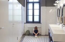 una alumna adolescente sentada en el piso del baño de su colegio