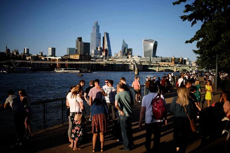 La gente disfruta de una tarde soleada junto al Támesis, con el skyline de la Ciudad de Londres de fondo.