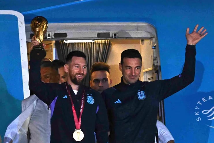El capitán y delantero argentino Lionel Messi (L) sostiene el Trofeo de la Copa Mundial de la FIFA junto con el entrenador argentino Lionel Scaloni cuando bajan de un avión al llegar al Aeropuerto Internacional de Ezeiza después de ganar el torneo de la Copa Mundial Qatar 2022 en Ezeiza, provincia de Buenos Aires, Argentina en diciembre 20, 2022.