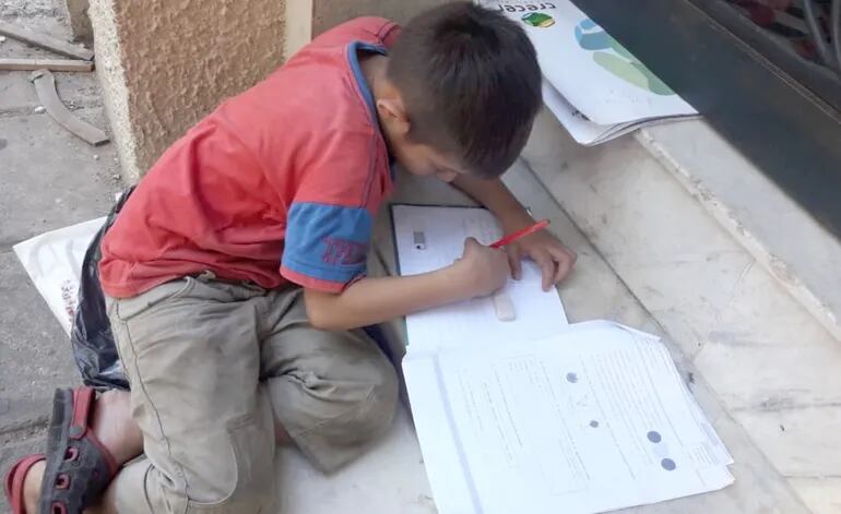 Sentado en una vereda del centro asunceno, un niño sigue su educación  con  la ayuda de fotocopias entregadas en su escuela.