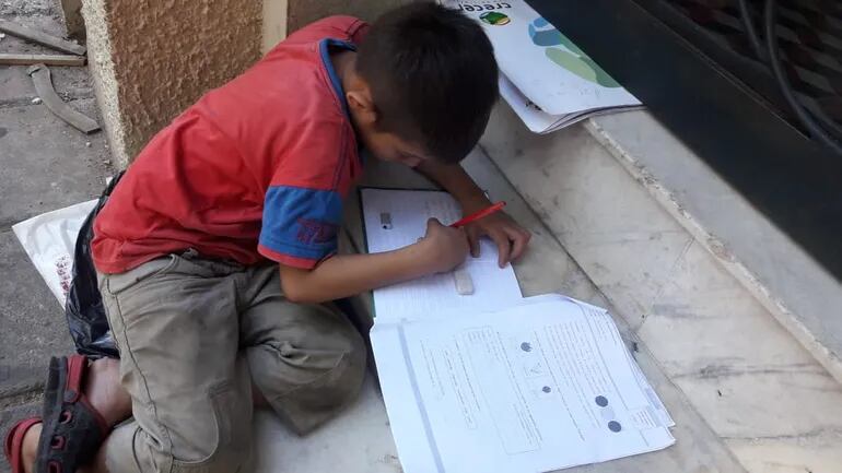 Un niño estudia con folletos en una vereda del centro asunceno.