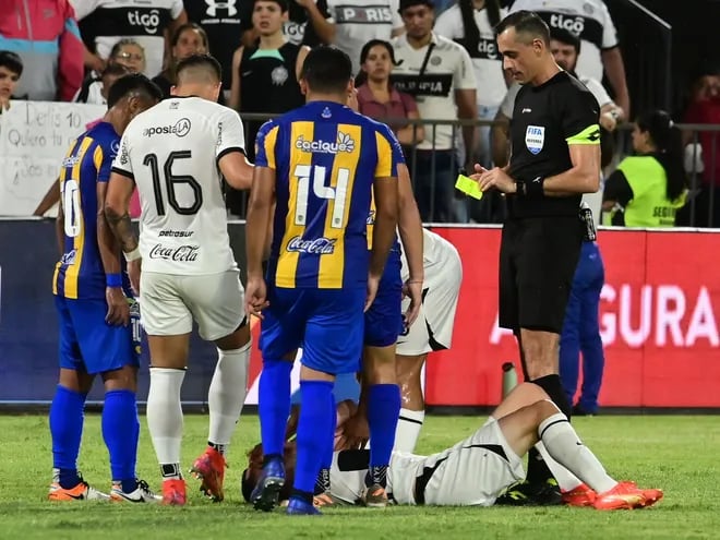 Diego Torres, jugador de Olimpia, tendido en el suelo y recibiendo asistencia médica después de la falta de Joel Jiménez de Sportivo Luqueño.