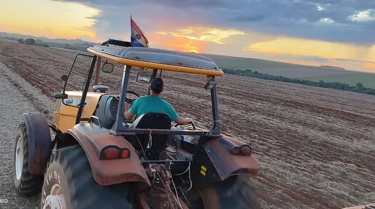 Un productor   realizando la siembra del maíz, mientras en el horizonte se ven nubes de lluvias en ciernes