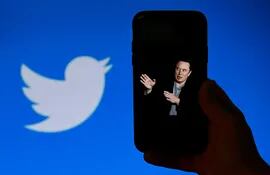(FILES) In this file photo taken on October 4, 2022, a phone screen displays a photo of Elon Musk with the Twitter logo shown in the background, in Washington, DC.