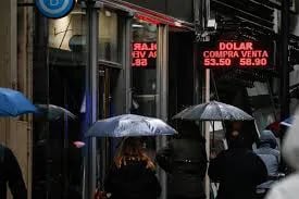 Transeúntes caminan bajo la lluvia frente a carteles que informan el precio del peso argentino sobre la moneda extranjera en Buenos Aires, Argentina. (Imagen de archivo EFE ).
