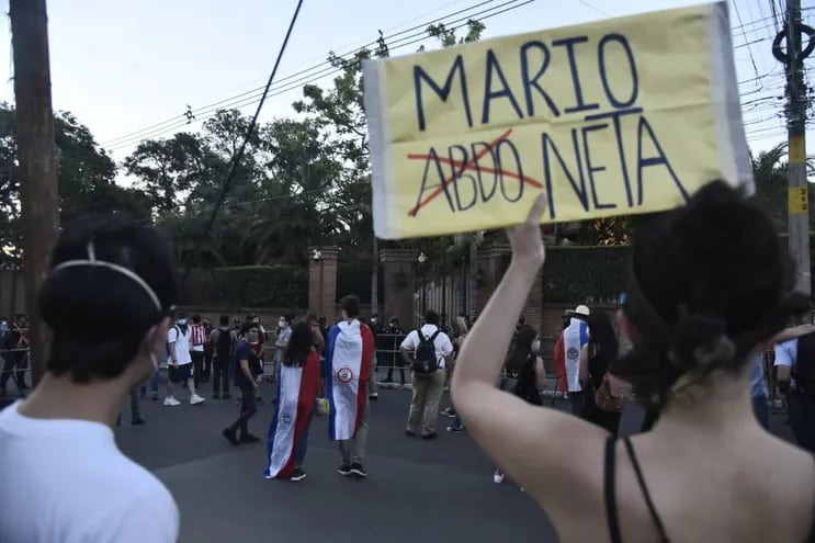 Una mujer sostiene un cartel que hace un juego con la combinación del nombre del presidente Mario Abdo y la palabra "marioneta", frente a la casa del expresidente Horacio Cartes.