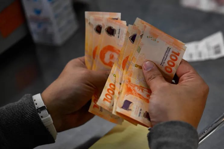 Un hombre cuenta mil billetes de pesos argentinos en Buenos Aires