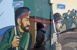 Una mujer camina frente a un mural que muestra a soldados de la Guardia Revolucionaria iraní, en Teherán.
