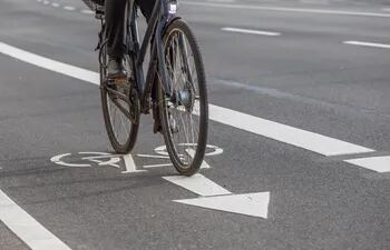 Un hombre pedalea una bicicleta por una bicisenda pintada en el asflato y señalizada con un dibujo de bicicleta y una flecha que indica el sentido del tráfico.