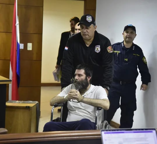Esposado y en silla de ruedas, Gregorio Papo Morales ingresa a la sala de juicios, conducido por un agente penitenciario.