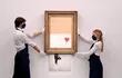Empleados de la galería posan junto al cuadro "El amor está en la papelera", del artista callejero anónimo Bansky, en la casa de subastas Sotheby's.