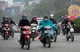 Personas protegidas con mascarillas viajan en motocicletas por una calle de Hanoi, Vietnam.